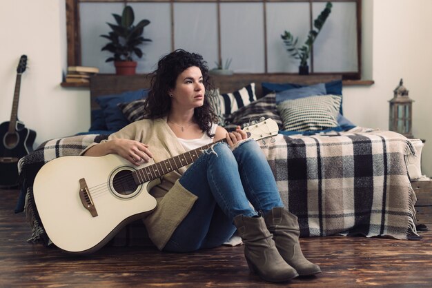 Mujer con guitarra apoyada contra cama