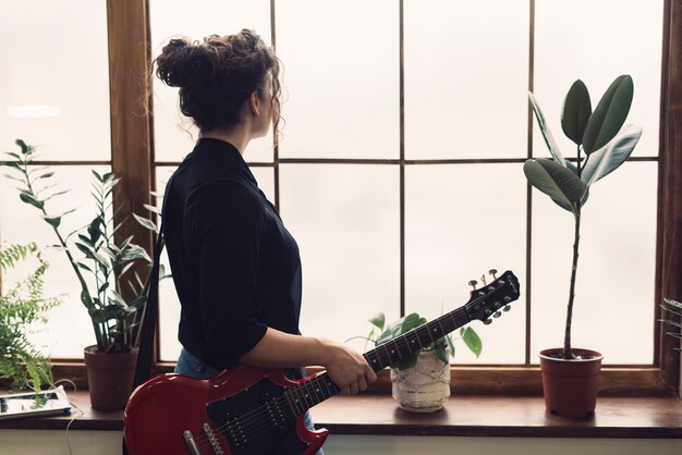 Mujer con guitarra roja mirando por ventana
