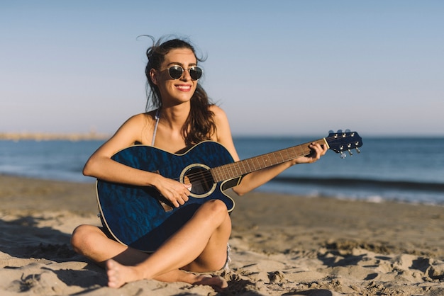 Mujer con guitarra sentada en la arena