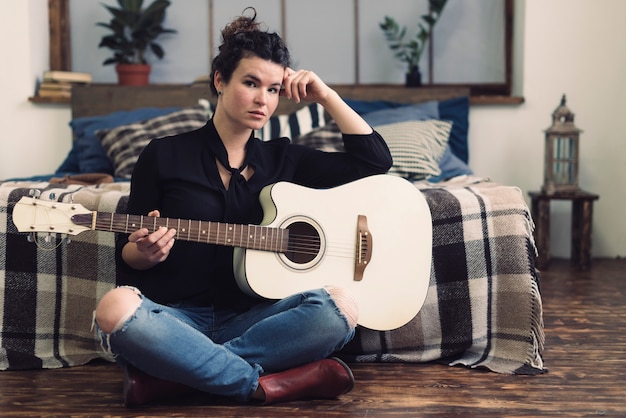 Mujer con guitarra sentada en su habitación