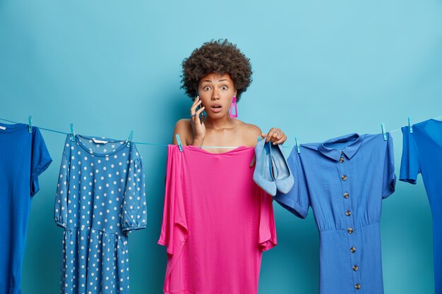 La mujer ha sorprendido a la expresión; no tiene tiempo para prepararse para la fiesta, elige vestirse para adaptarse a los zapatos nuevos, tiene una conversación telefónica aislada en azul