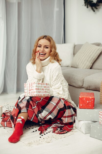 Mujer en una habitación. Rubia con un suéter blanco. Señora cerca del árbol de Navidad.