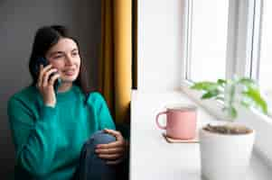 Foto gratuita mujer hablando por su teléfono inteligente en casa durante la cuarentena