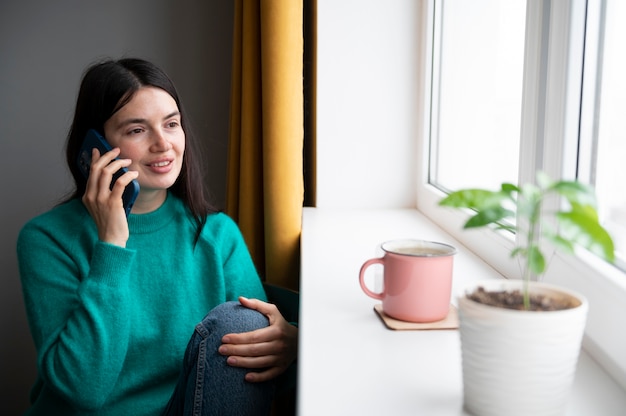 Mujer hablando por su teléfono inteligente en casa durante la cuarentena