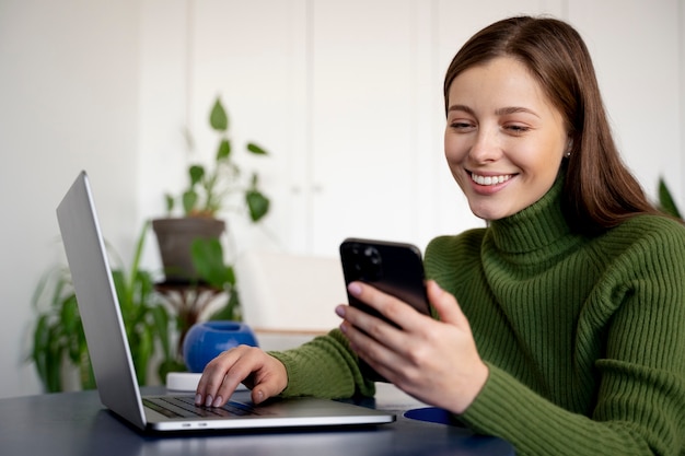 Mujer hablando por su teléfono inteligente usando la función de manos libres y escribiendo algo en su computadora portátil