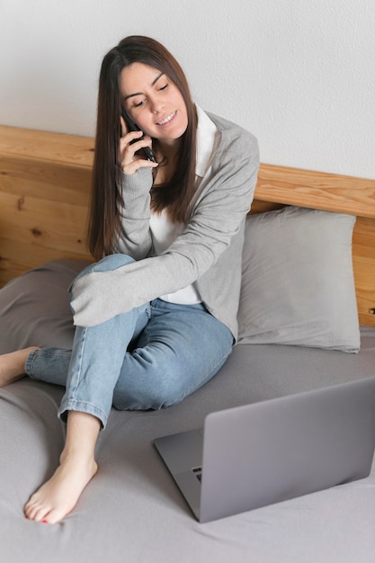 Mujer hablando por teléfono cerca de la computadora portátil en la cama