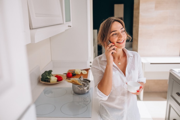 Mujer hablando por teléfono en la cocina y preparando el desayuno