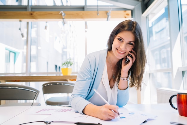 Foto gratuita mujer hablando por teléfono y corrigiendo gráficos