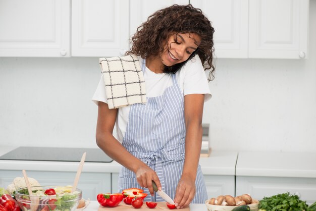 Mujer hablando por teléfono y cortando tomates