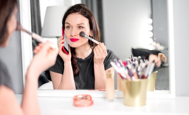 Mujer hablando por teléfono y haciendo maquillaje