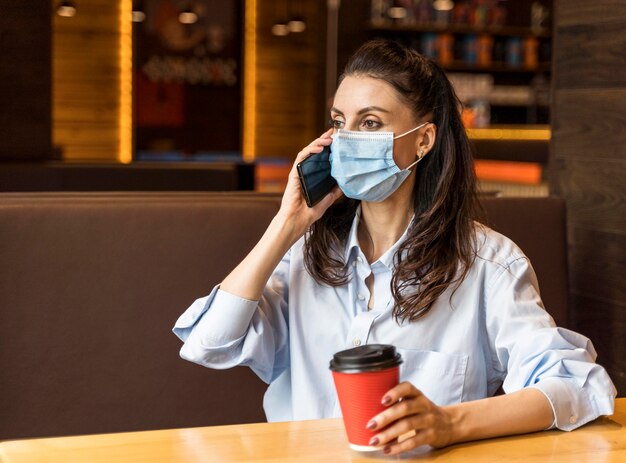 Mujer hablando por teléfono en el interior mientras usa una mascarilla