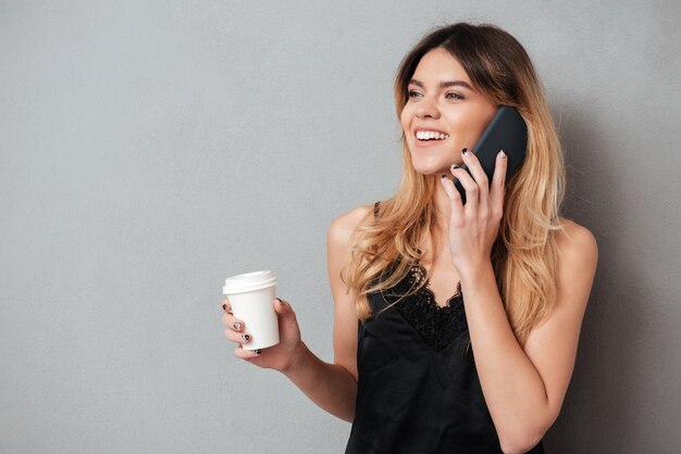 Mujer hablando por teléfono mientras bebe para ir a tomar una taza de café