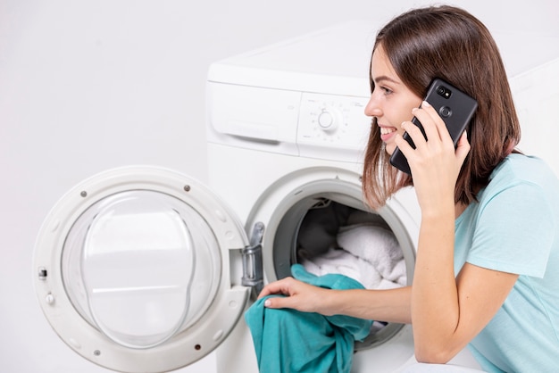 Mujer hablando por teléfono mientras lava la ropa