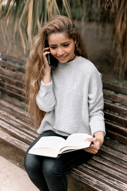 Foto gratuita mujer hablando por teléfono mientras sostiene un libro