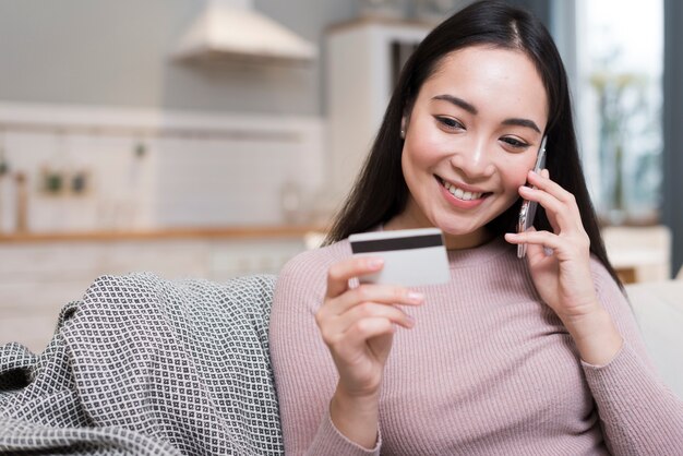 Mujer hablando por teléfono mientras sostiene la tarjeta de crédito