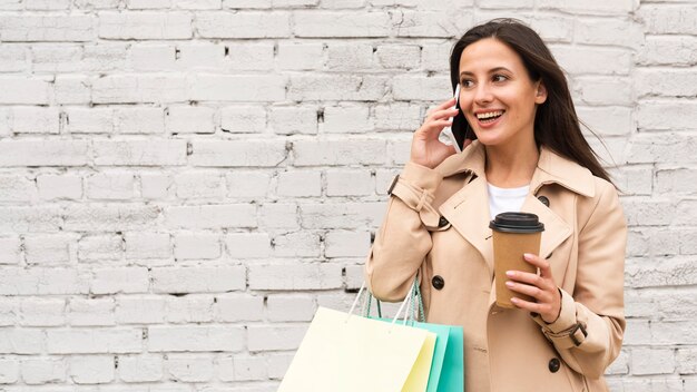 Mujer hablando por teléfono mientras toma un café y sostiene bolsas de la compra.