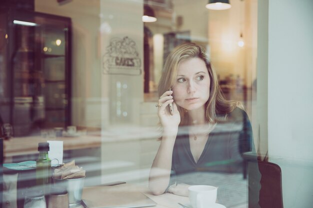 Mujer hablando por teléfono y mirando por la ventana en el café