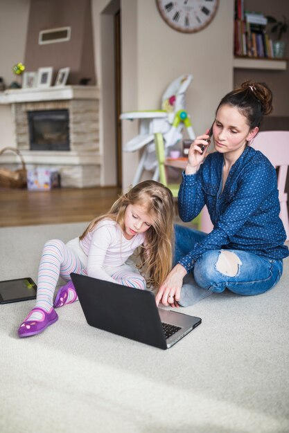 Mujer hablando por teléfono móvil mientras su hijo mirando la pantalla del portátil