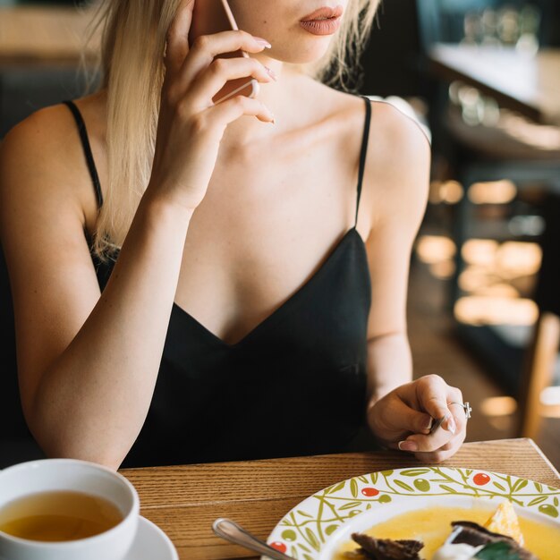 Mujer hablando por teléfono móvil mientras toma el desayuno en la cafetería