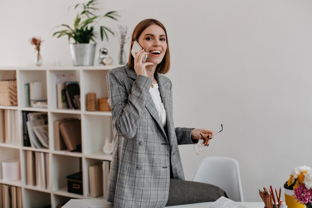Mujer hablando por teléfono con una sonrisa amistosa mientras está sentada en su lugar de trabajo