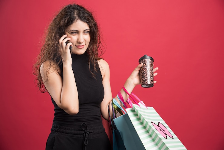 Foto gratuito mujer hablando por teléfono con taza y bolsas sobre fondo rojo. foto de alta calidad