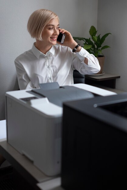 Mujer hablando por teléfono en el trabajo junto a la impresora