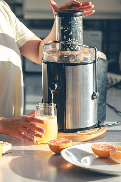 Una mujer hace jugo de naranja en casa en la cocina con un exprimidor eléctrico
