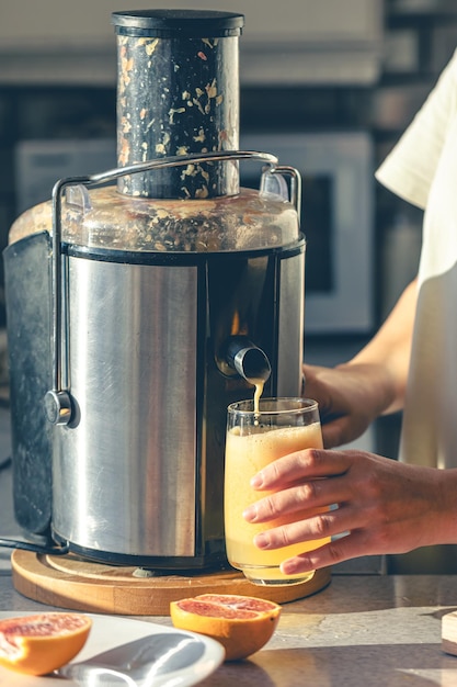 Foto gratuita una mujer hace jugo de naranja en casa en la cocina con un exprimidor eléctrico