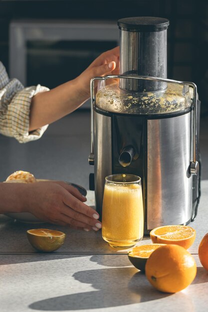 Foto gratuita una mujer hace jugo de naranja en casa en la cocina con un exprimidor eléctrico