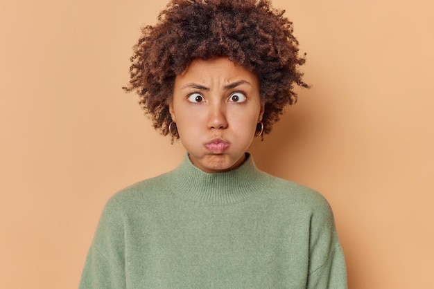 mujer hace pucheros labios sopla mejillas hace muecas hilarantes aguanta el aliento cruza los ojos vestidos con un jersey casual aislado en beige intenta divertir a alguien