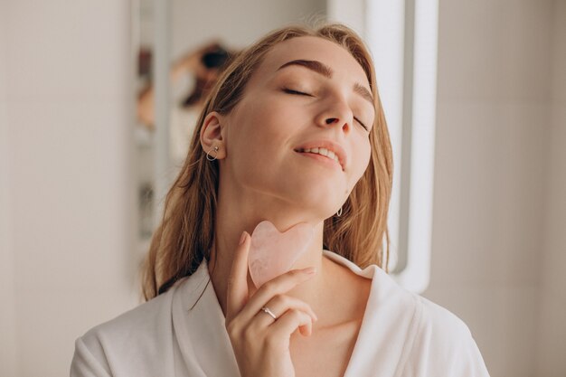 Mujer haciendo auto masaje con piedra gua sha de cuarzo rosa