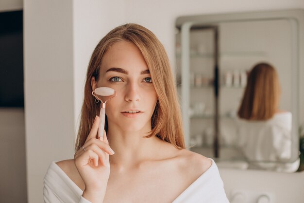 Mujer haciendo auto masaje con rodillo facial de cuarzo rosa