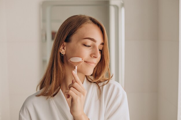 Mujer haciendo auto masaje con rodillo facial de cuarzo rosa