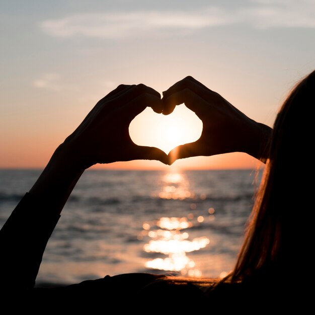 Mujer haciendo un corazón al atardecer