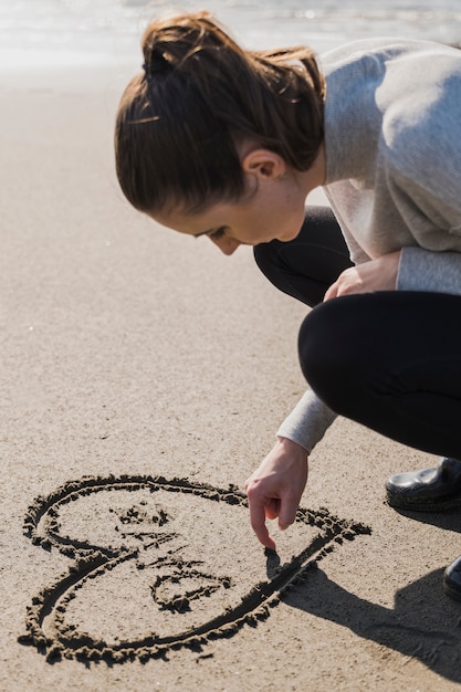 Mujer haciendo corazón sobre arena mojada