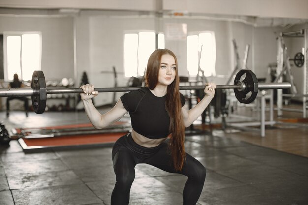 Mujer haciendo ejercicio con barra. El uso de ropa deportiva negra.