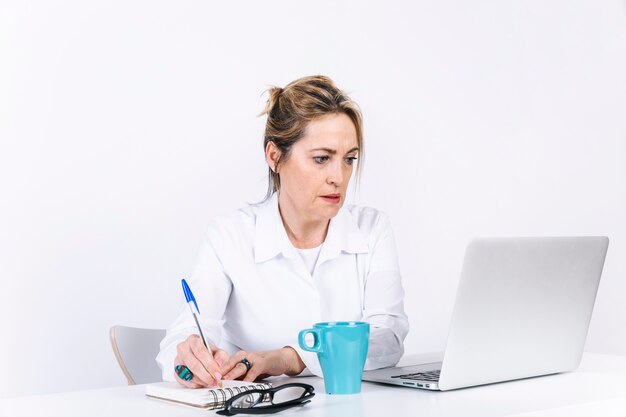 Mujer haciendo notas cerca de la computadora portátil