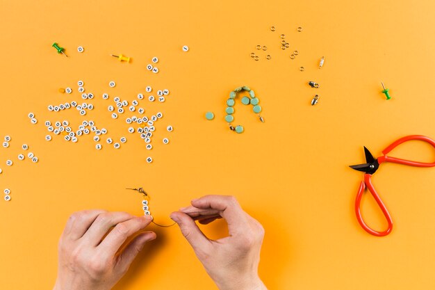 Mujer haciendo pulsera de abalorios de letras sobre fondo amarillo