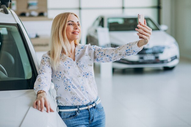 Mujer haciendo selfie en el auto en una sala de exposición de automóviles