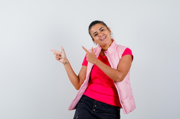 Mujer haciendo signo de pistola de dedo en camiseta, chaleco y mirando confiado