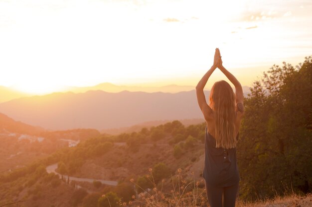 Mujer haciendo yoga mientras ve la puesta de sol con espacio de copia