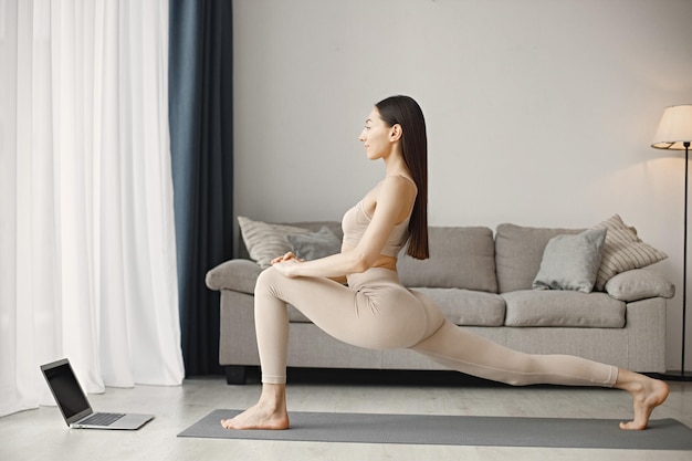 Mujer haciendo yoga mientras ve tutoriales de entrenamiento en línea en una computadora portátil en casa
