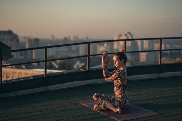 Mujer haciendo yoga en el techo de un rascacielos en la gran ciudad.