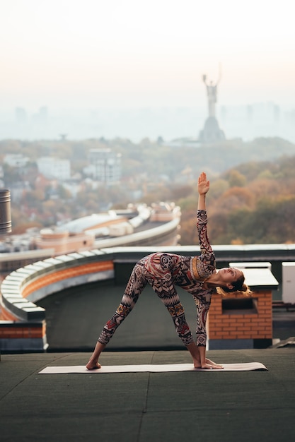 Mujer haciendo yoga en el techo de un rascacielos en la gran ciudad.