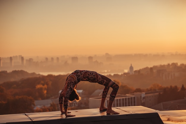 Mujer haciendo yoga en el techo de un rascacielos en la gran ciudad.