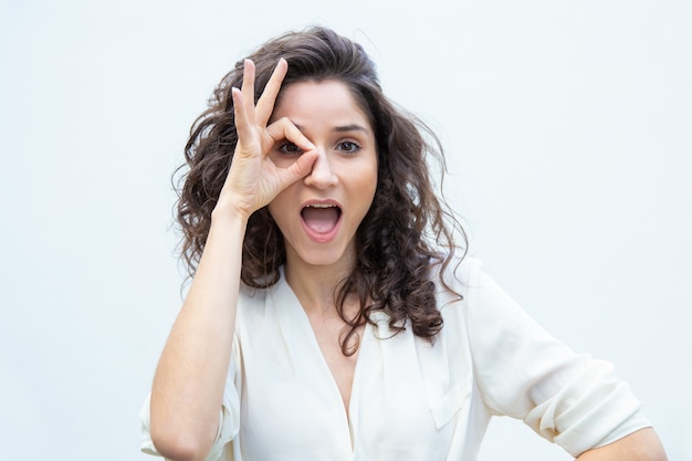 Mujer hermosa alegre con la boca abierta aplicando la mano al ojo