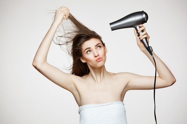 Mujer hermosa alegre en toalla sonriendo riendo cantando con secador de pelo haciendo cara divertida. Spa de belleza y cosmetología.