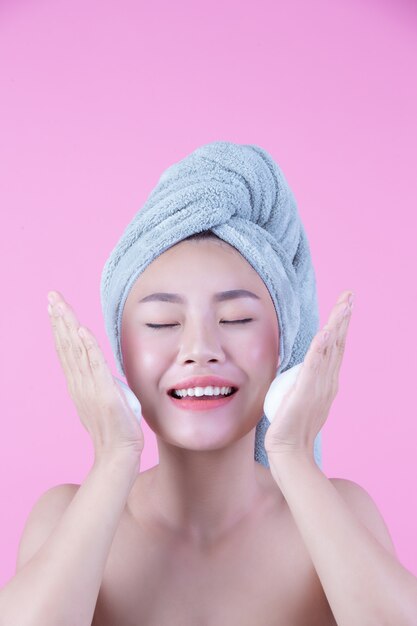 La mujer hermosa Asia se está lavando la cara en fondo rosado.