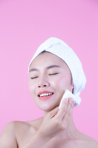 Mujer hermosa asiática que limpia la cara en un fondo, una cosmetología y un balneario rosados.