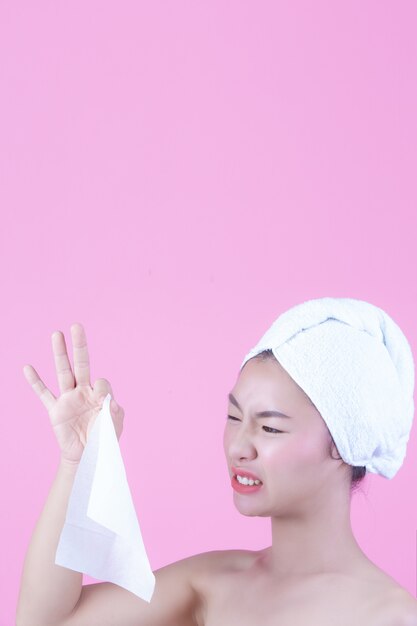 Mujer hermosa asiática que limpia la cara en un fondo, una cosmetología y un balneario rosados.